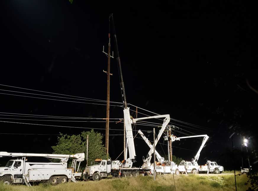 several bucket trucks working on a line at night